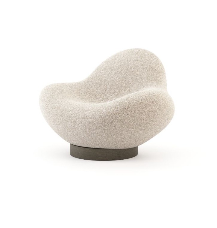 La poltrona Stone, caratterizzata da una silhouette morbida e arrotondata e da un rivestimento beige testurizzato, poggia su una base circolare scura in un ambiente minimalista, mettendo in risalto la sua forma scultorea ispirata alla pietra.