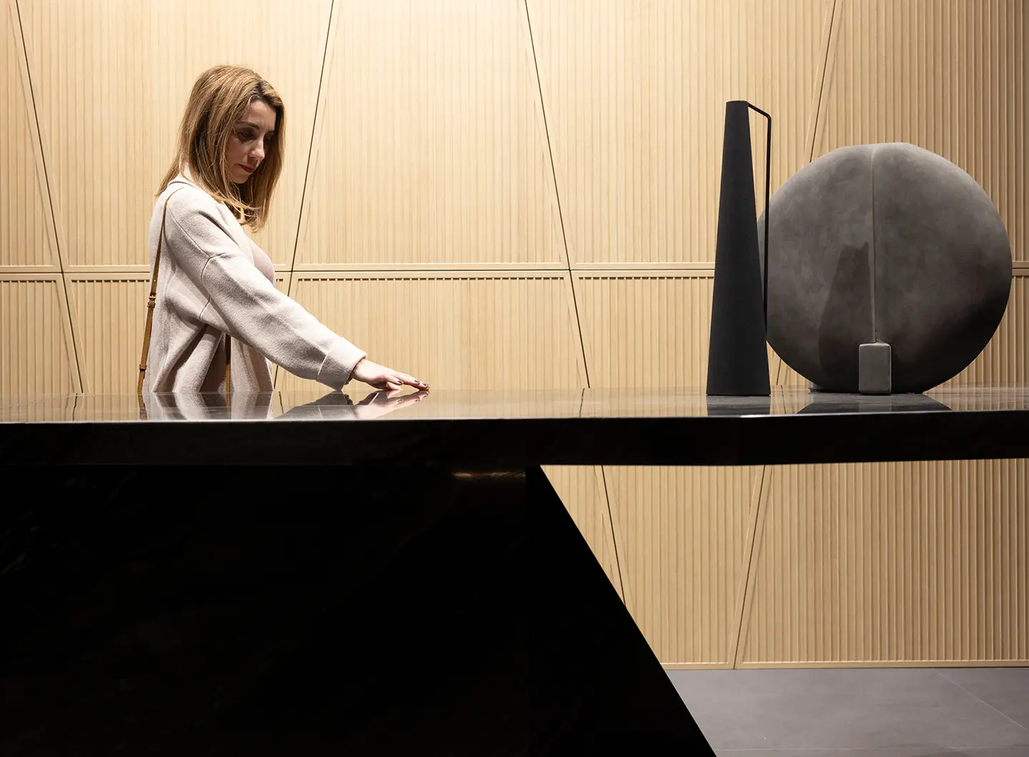 Against a light wooden wall, a girl touches a glossy black lacquered counter.