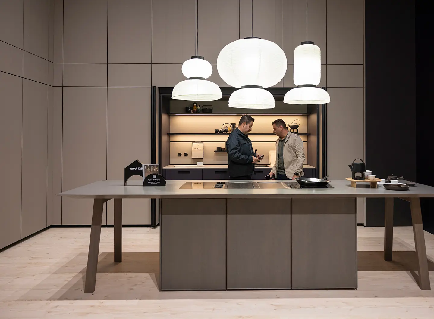 In the background, a matte beige full-height kitchen unit with concealed doors. Centre kitchen table with hob