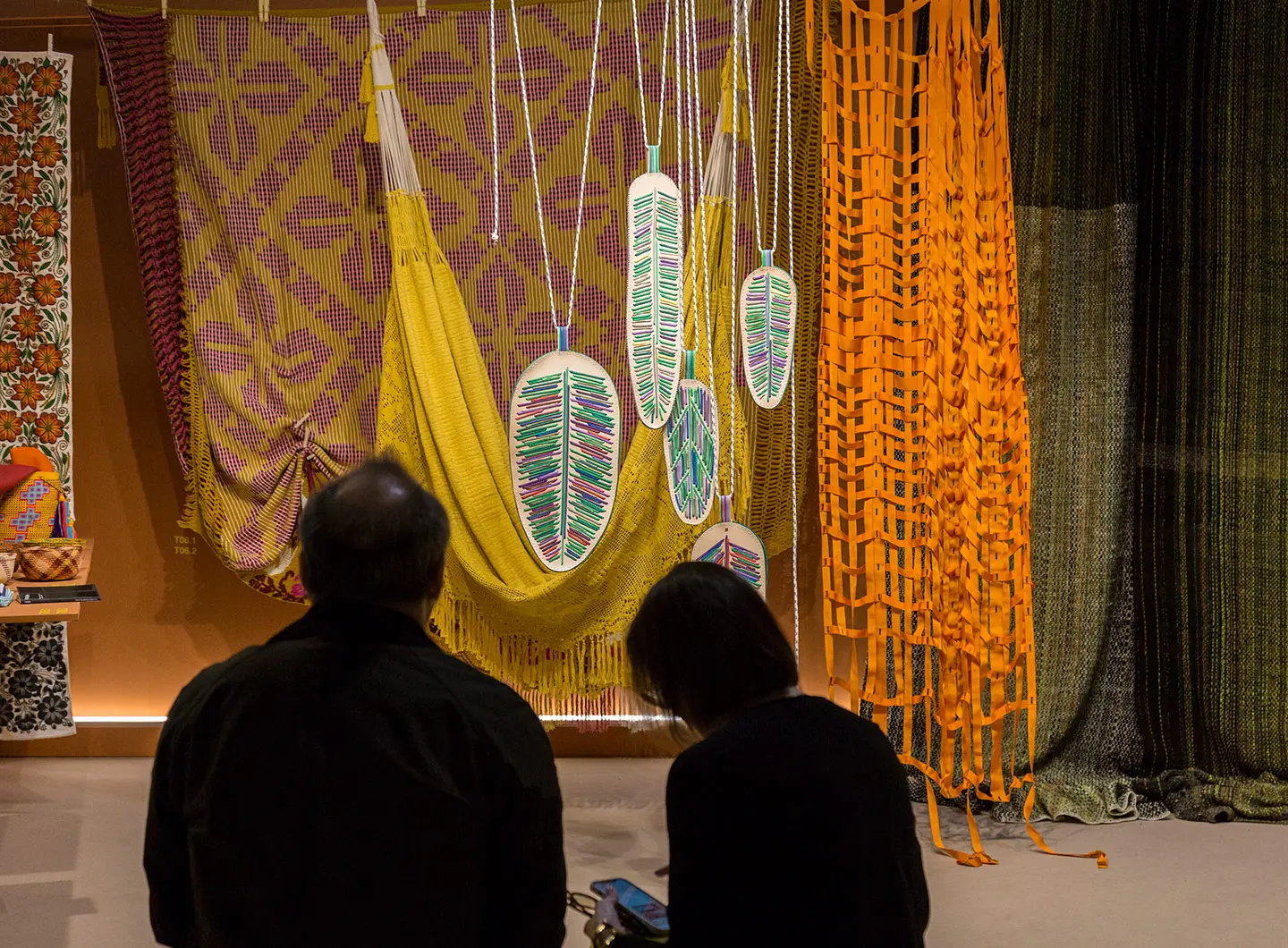 Two people observing a stand with colourful fabric elements and leaf-shaped objects