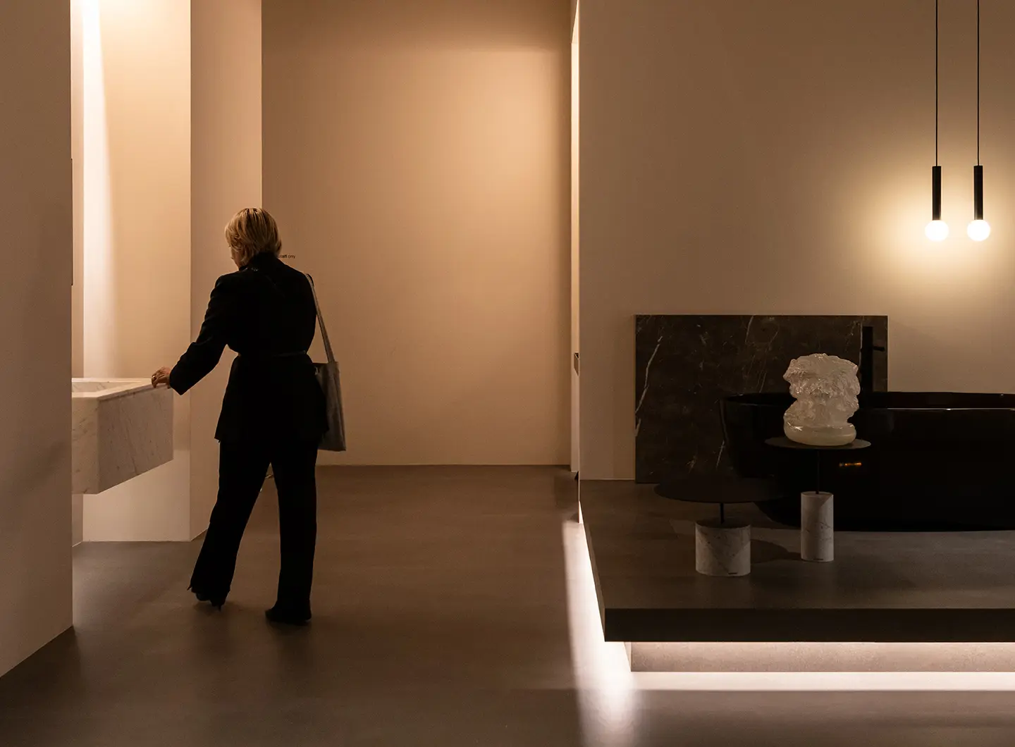 Woman from behind touching white sink, and black marble slab and basin with marble tables