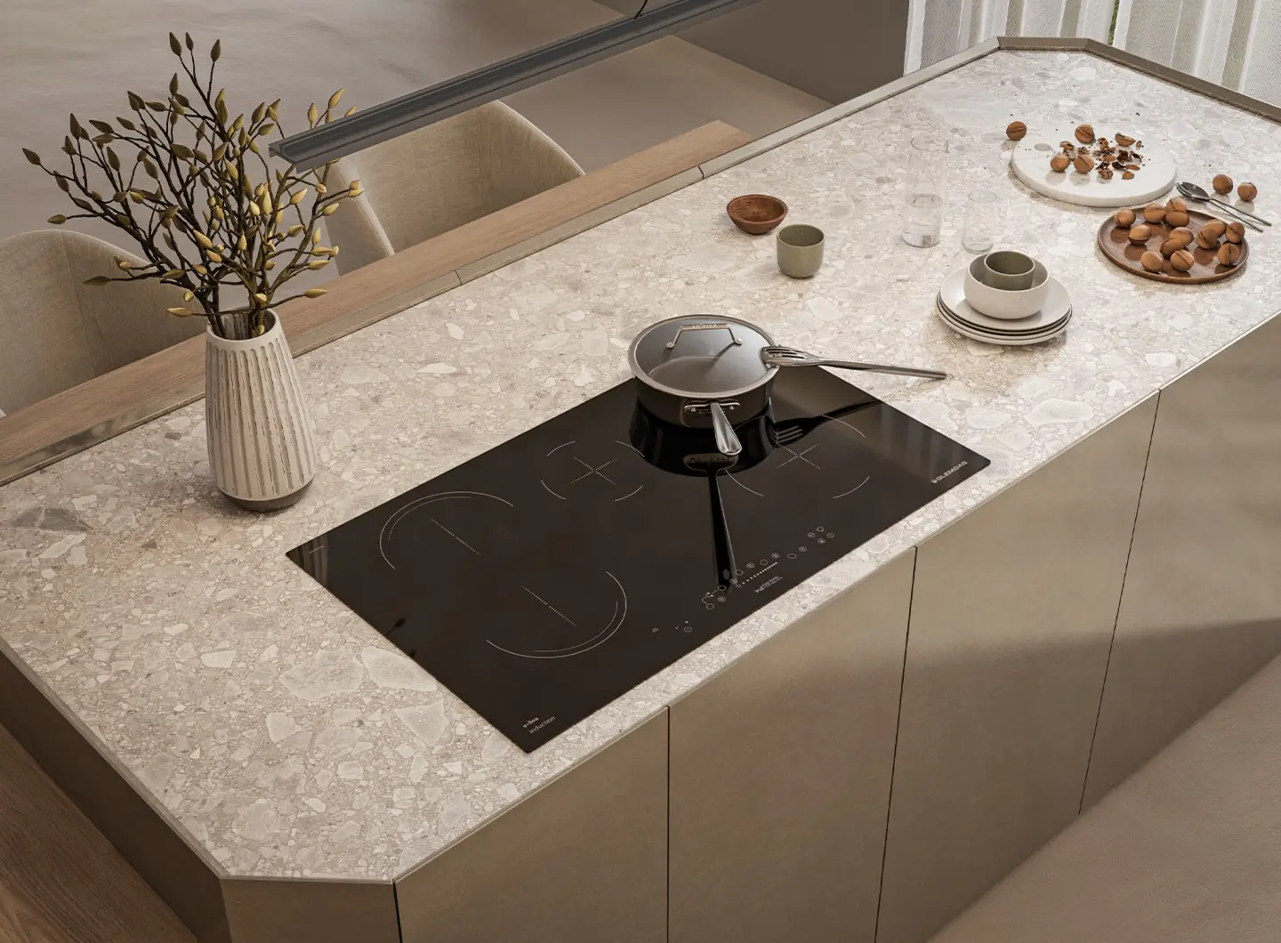 Inquadratura dall'alto di un'ampia isola da cucina con installato un piano cottura a induzione in vetro nero da 90 cm con 5 zone di cui una bridge e comandi touch. Sulla superficie sono disposti piatti, ciotole in ceramica e una pentola in acciaio, creando un'atmosfera conviviale e raffinata.