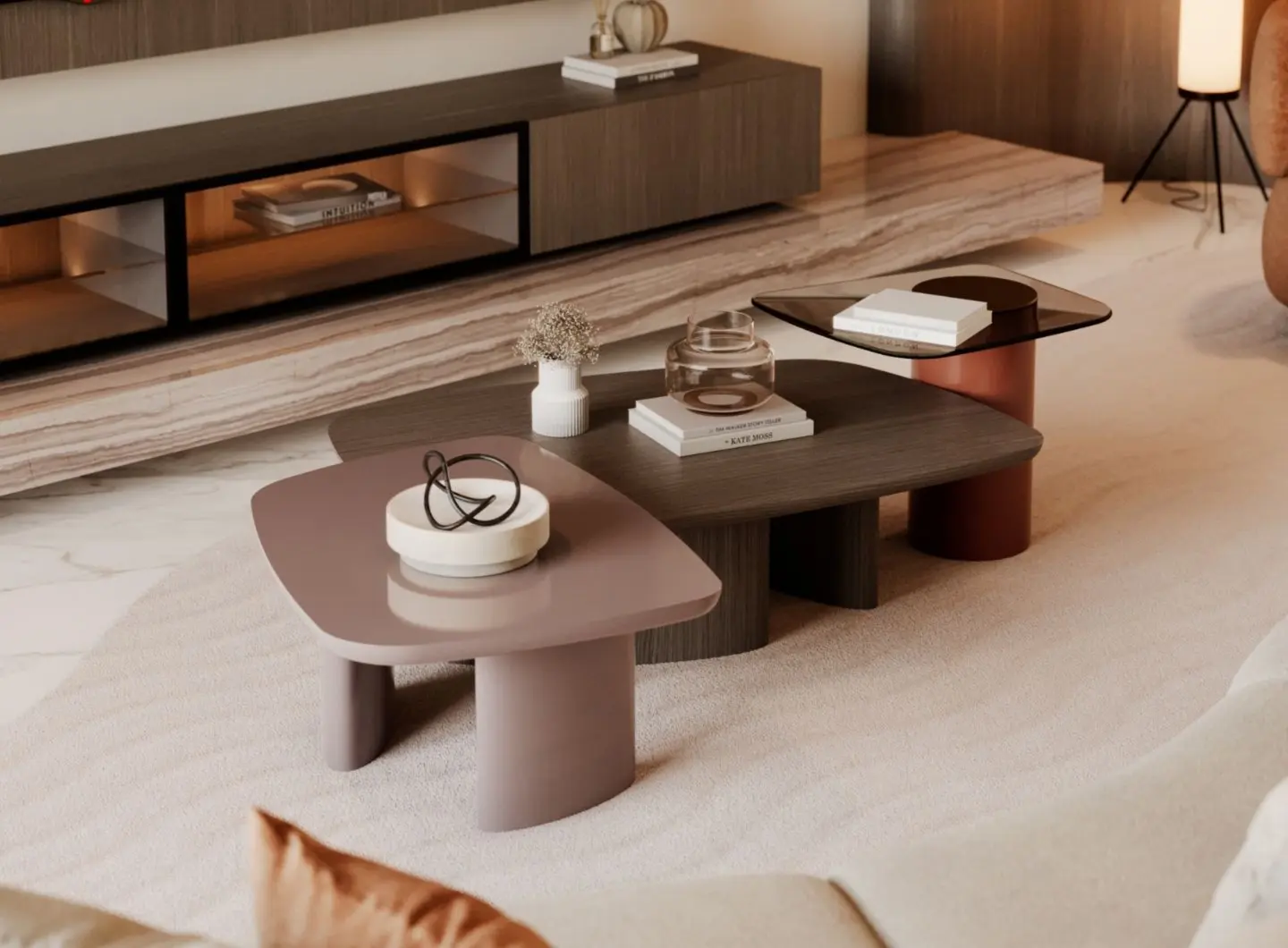 Il Tavolino da caffè Dolomites si presenta come un set di tre tavolini dalle forme arrotondate realizzati con materiali misti, tra cui un piano color malva, uno in legno scuro e uno in vetro colorato, sostenuti da una base cilindrica color rame; sono disposti su un tappeto chiaro, con oggetti decorativi e libri nelle vicinanze, e presentano dettagli in ottone nelle basi dei tavolini.
