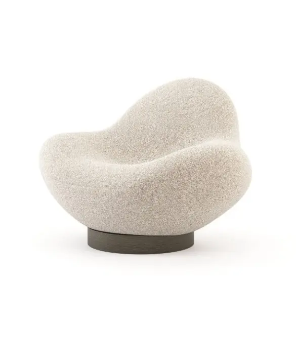 La poltrona Stone, caratterizzata da una silhouette morbida e arrotondata e da un rivestimento beige testurizzato, poggia su una base circolare scura in un ambiente minimalista, mettendo in risalto la sua forma scultorea ispirata alla pietra.