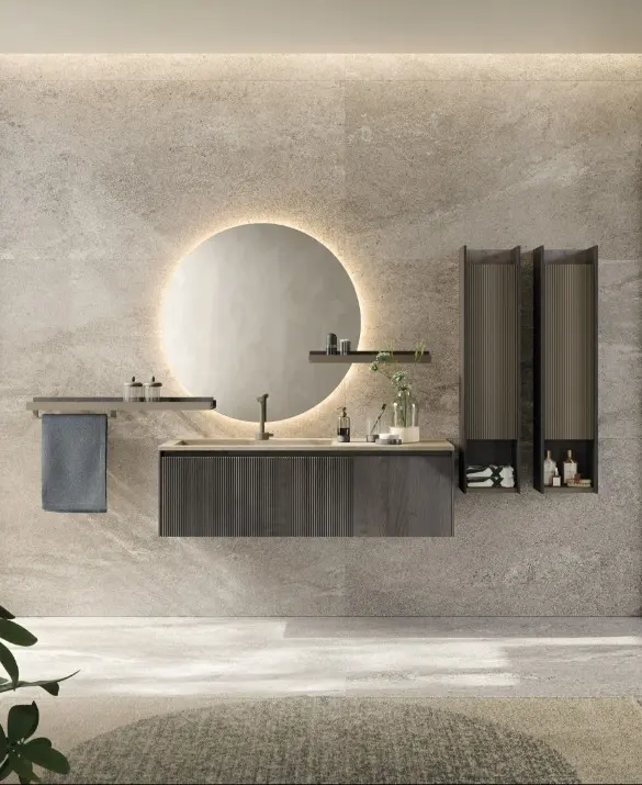 Bagno D'Art. Base portalavabo con anta plissé e anta liscia in rovere fumo, pensili con anta plissé in laccato lava opaco e struttura in rovere fumo, piano lavabo in gres porcellanato Fokos Roccia, mensole bicolor in laccato lava opaco e rovere fumo. Barra porta asciugamani, specchio tondo con led perimetrale.